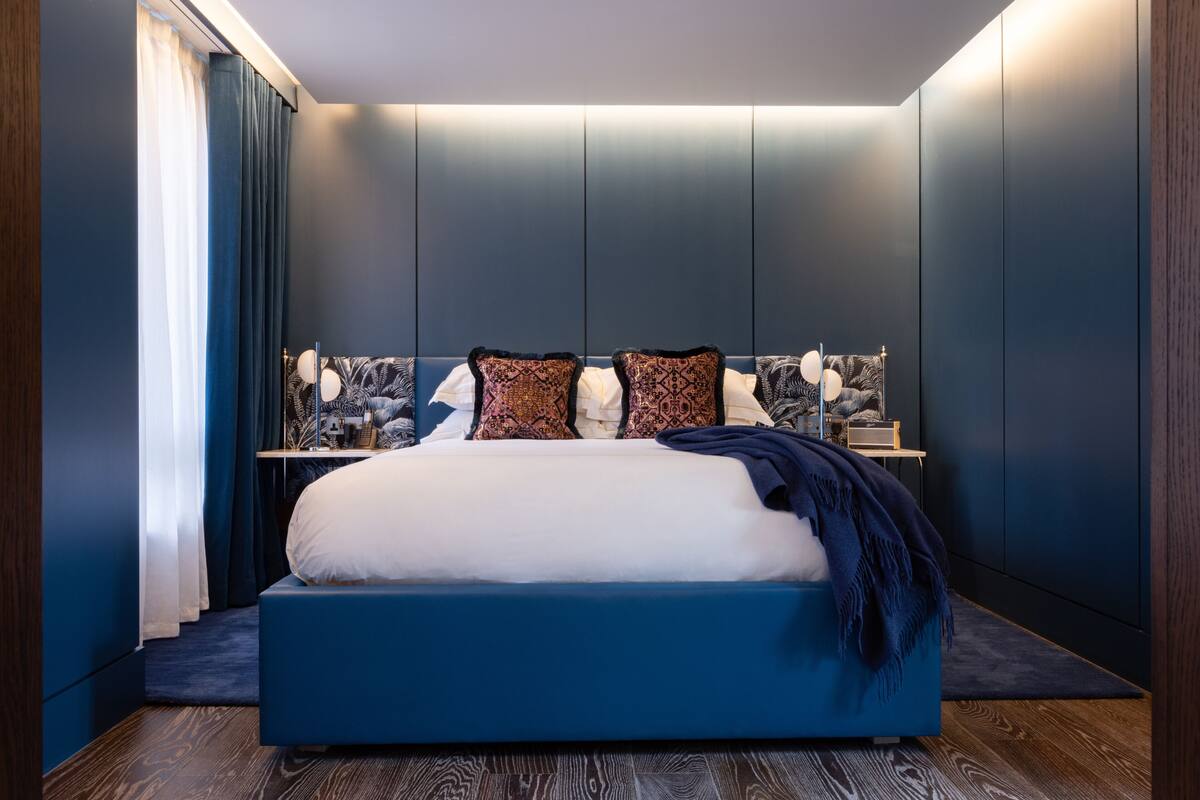 A modern bedroom with a large bed, dark walls, and a bedside table with decorative items.