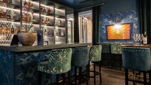 Eine Bar mit einer Marmorplatte, grünen Sitzhocker und Regalen voller Spirituosenflaschen.