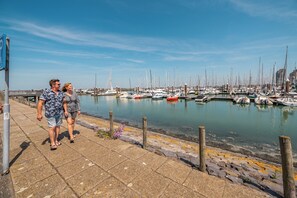 A marina with boats docked, a clear sky, and a couple walking on the promenade. - Pure luxury and space for up to 6 persons (Nieuwvliet)