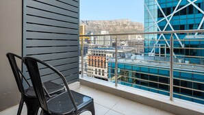 A balcony with a view of a cityscape, including a modern building with blue glass and a mountain in the background. - Modern Designer Apartment in Bree Street (Cape Town)
