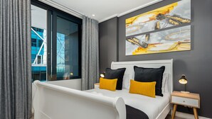 A modern bedroom with a white bed, grey curtains, and a city view. - Modern Designer Apartment in Bree Street (Cape Town)