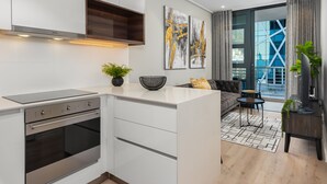 A modern kitchen with built-in appliances, a dining area with a sofa and coffee table, and a view of the city through large windows. - Modern Designer Apartment in Bree Street (Cape Town)