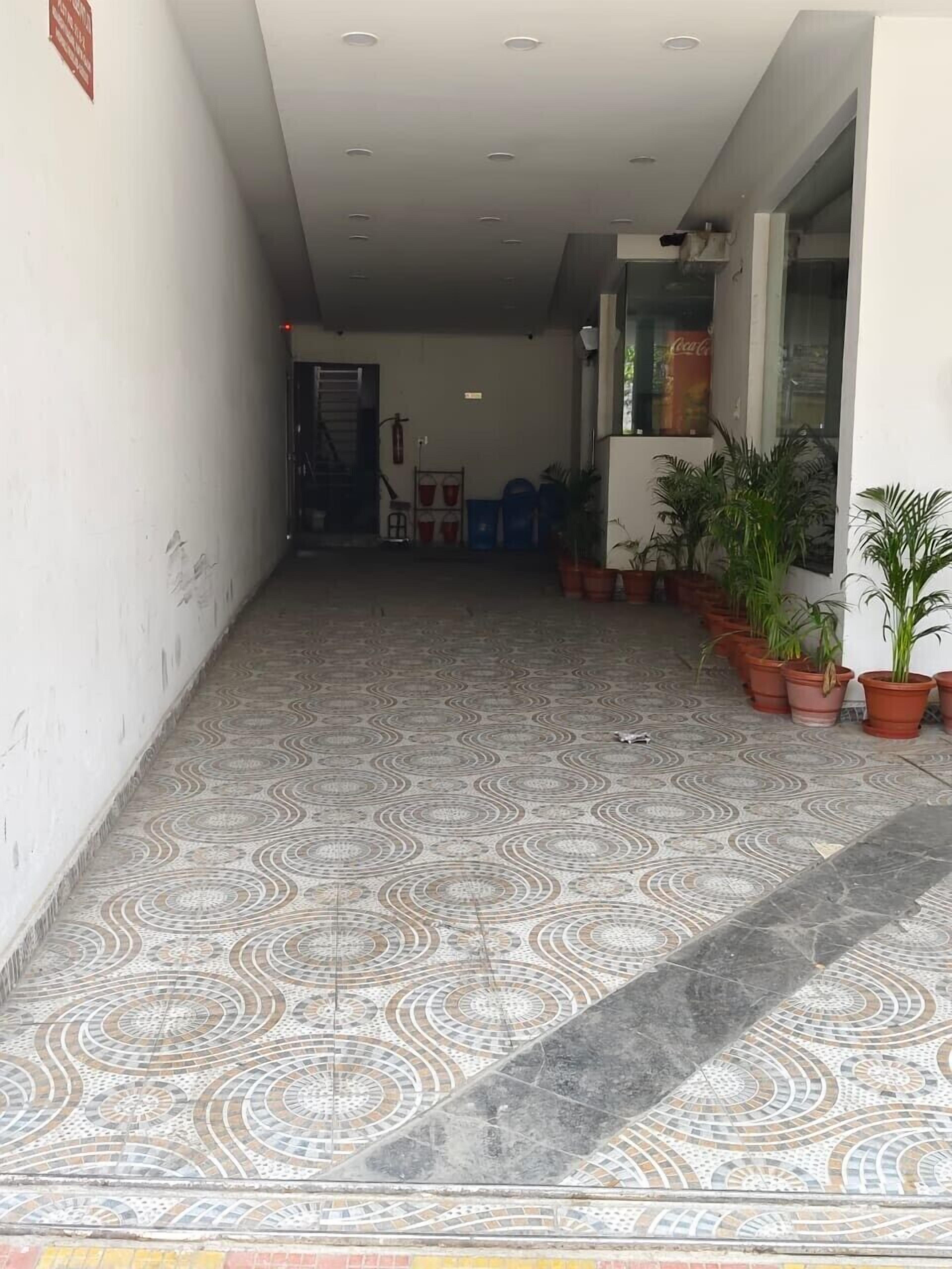 A hallway with patterned tile flooring, potted plants, and a Coca-Cola advertisement on the wall.
