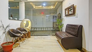 A modern living room with a brown leather sofa, two black chairs, a large decorative mirror, and a potted plant. - Treebo Royal Empire Adarsh Nagar, Chandigarh (Kharar)