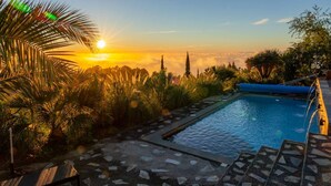 A swimming pool with a view of the sunset, surrounded by palm trees and a stone pathway. - Absolute Ruhe und Alleinlage Über den Wolken, Pool - Panorama Suite El Mirador (Las Tricias)