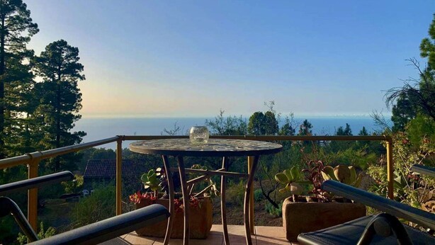A terrace with a table and chairs, overlooking a scenic landscape with trees and a distant view.