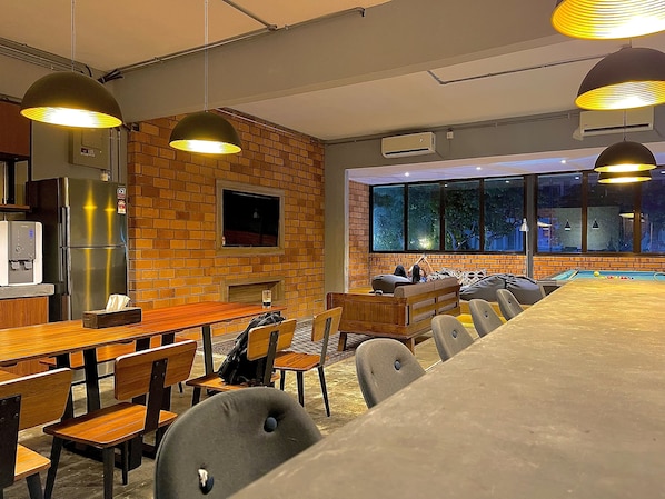 A modern dining area with a long wooden table, multiple chairs, and pendant lighting.