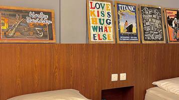 A hotel room with two beds, wooden headboard, and wall-mounted posters including 'Harley Davidson' and 'Love Kiss Hug What Else'.