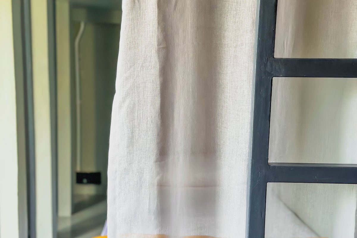 A window with a sheer curtain and a view of a hallway with a yellow object on the floor.