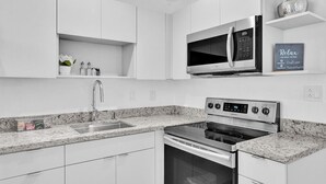 Una cocina moderna con armarios blancos, un microondas de acero inoxidable, un horno y una encimera de granito.