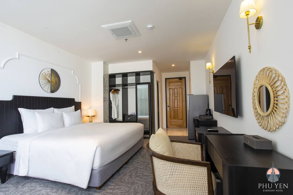 Een hotelkamer met een groot bed, een bureau, een stoel, een spiegel en een wandklok.