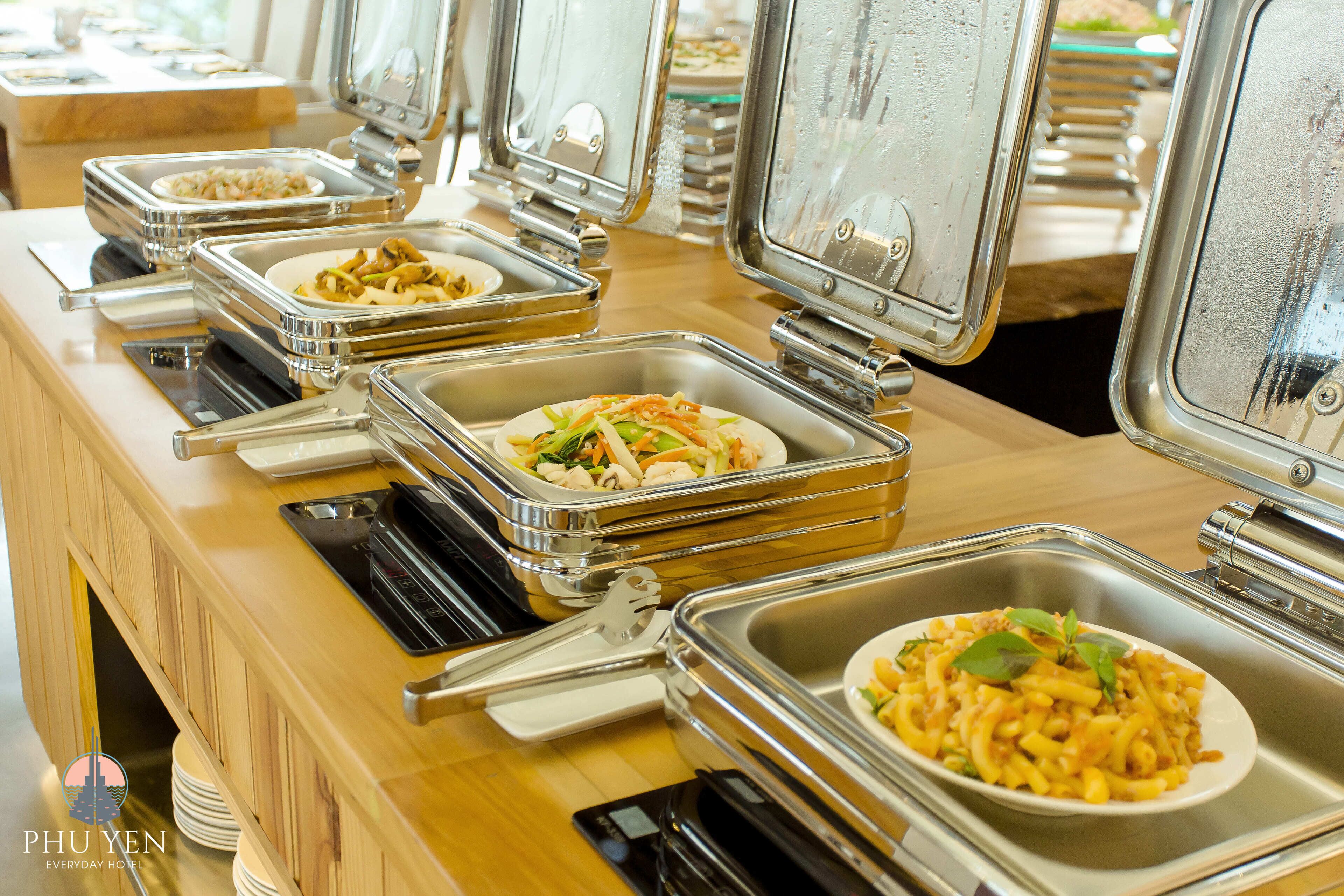 A buffet setup with multiple self-service food stations, each with a metal tray and a plate.