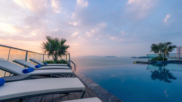 A poolside area with lounge chairs and palm trees, overlooking a body of water. - Phú Yên Everyday Hotel (Tuy Hoa)