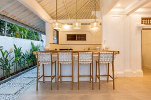A bar area with a high ceiling, wooden stools, and pendant lighting.