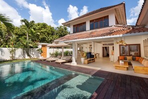 Een modern huis met een zwembad, buitenmeubels en een overdekt terras.