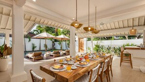 A spacious dining area with a long wooden table, multiple chairs, and hanging pendant lights.