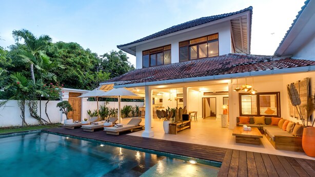 A modern house with a swimming pool, outdoor seating, and a well-lit patio area.