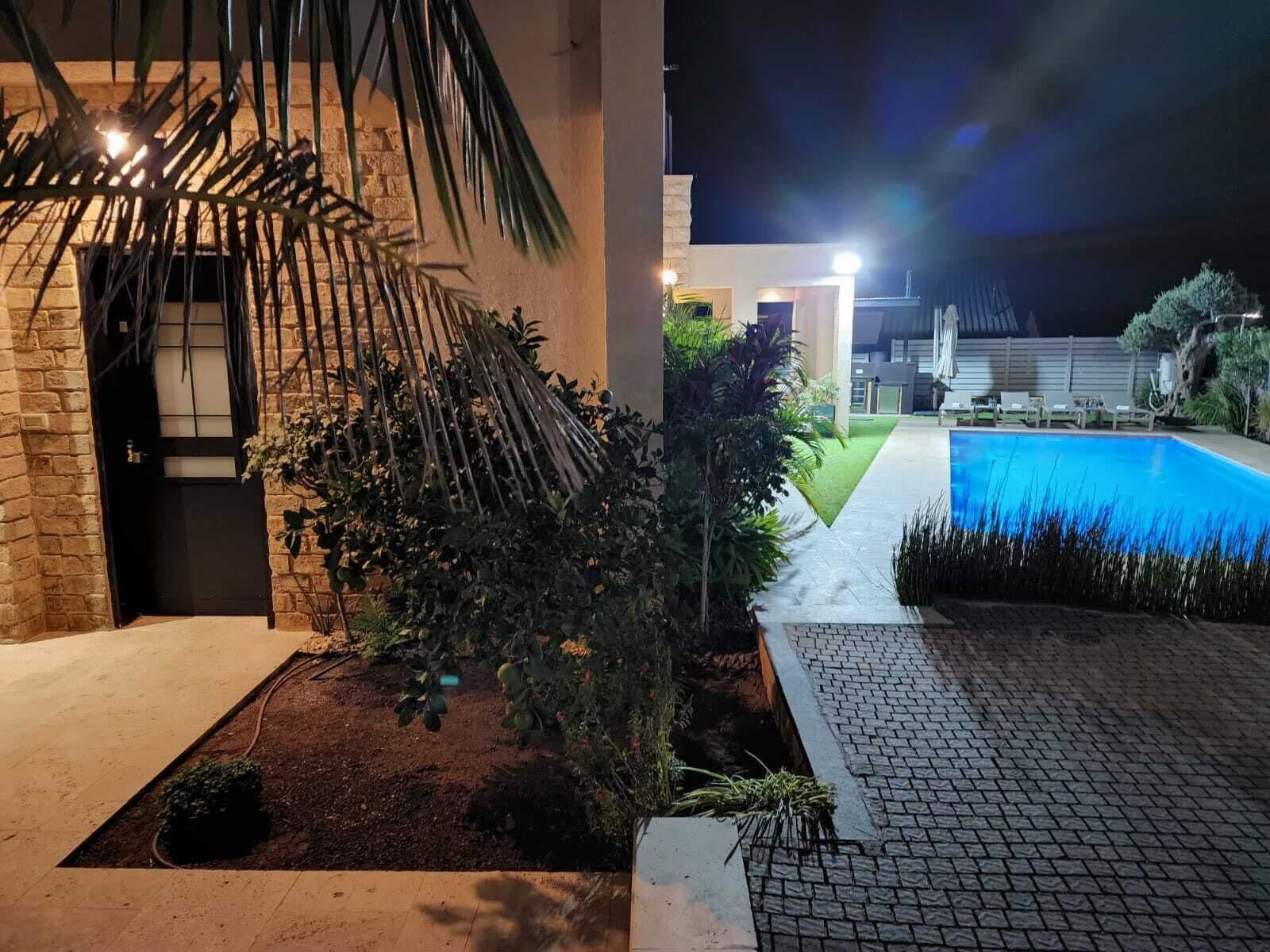 Ett väl upplyst utomhusområde med en swimmingpool, en stenmur och en mängd olika växter.