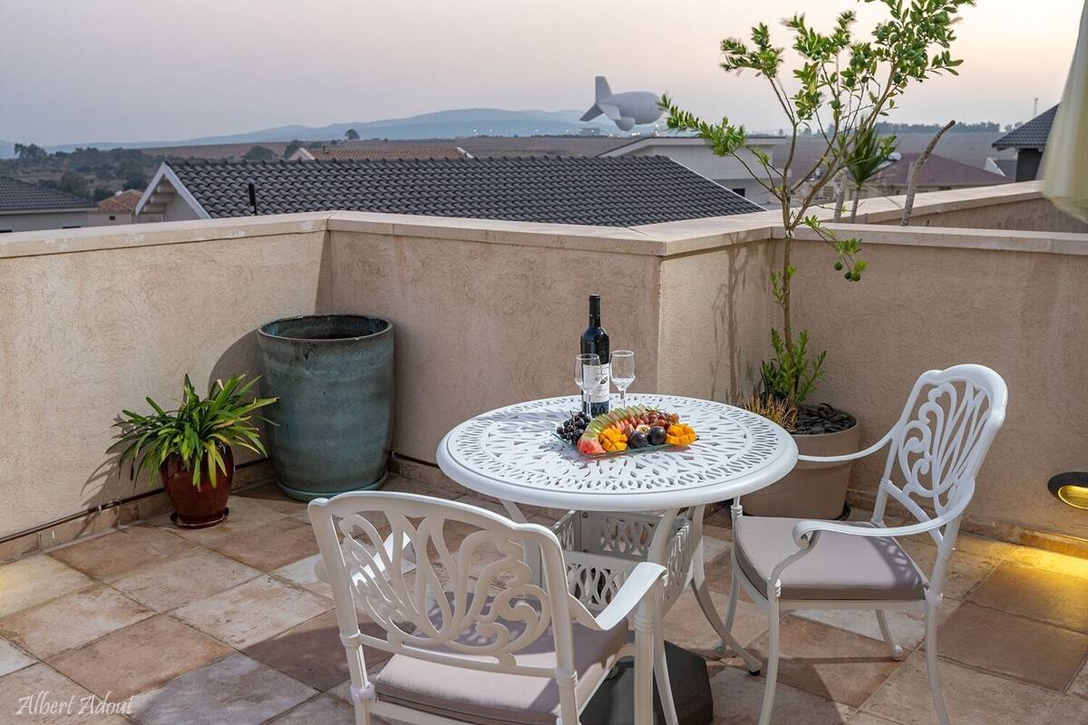 A terrace with a round table, two chairs, a bottle of wine, and a fruit platter.