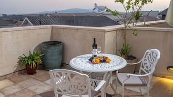 A terrace with a round table, two chairs, a bottle of wine, and a fruit platter.