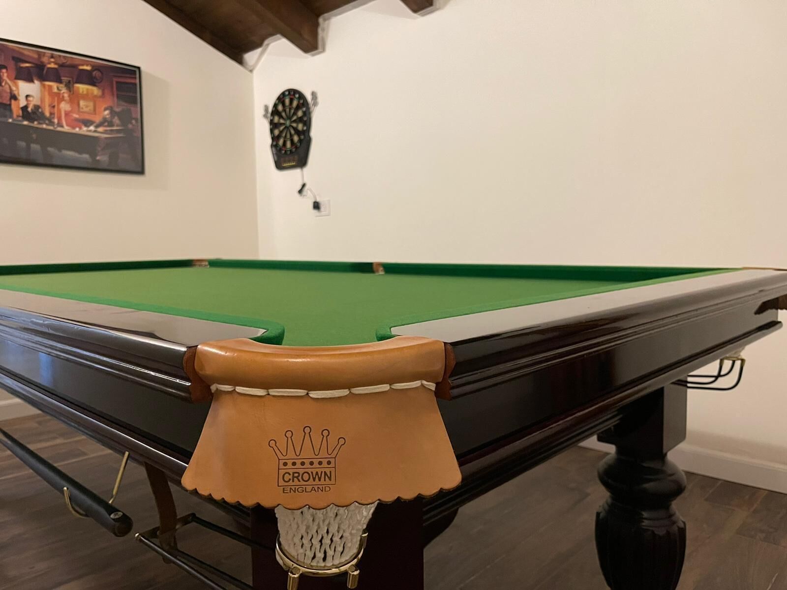 Una mesa de billar con un bolso de cuero marrón encima, un dardo en la pared y una foto enmarcada sobre la mesa.