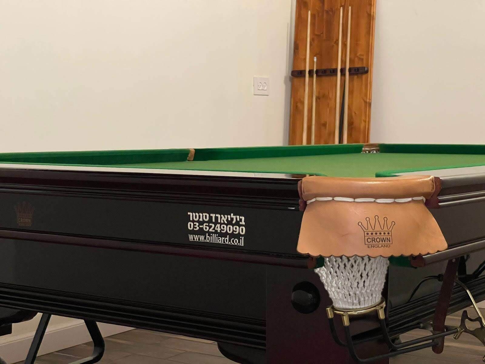 A pool table with a green felt surface, a black table base, and a white cloth with a brown leather edge. There is a logo on the table base and a website address.