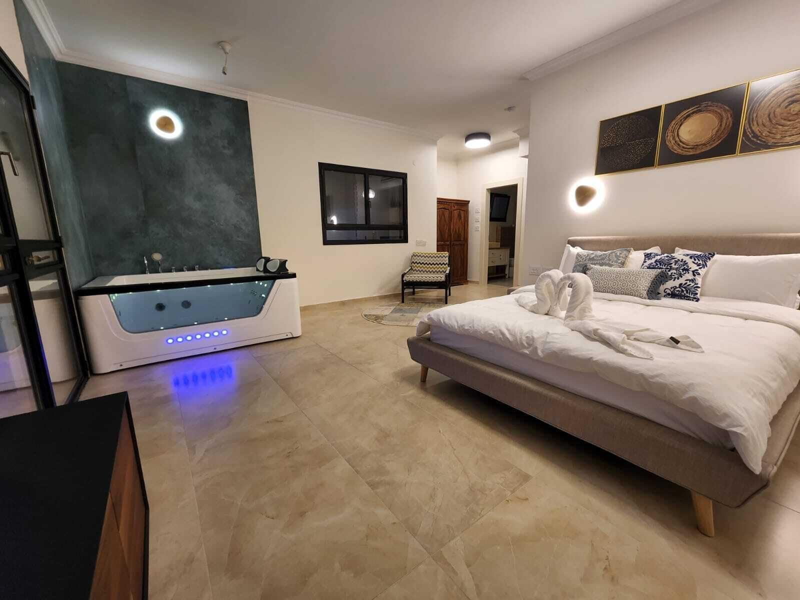 A modern bedroom with a large bed, a built-in bathtub, and a small seating area.