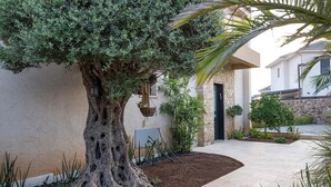 A well-maintained garden with a large tree, a stone wall, and a pathway leading to a building entrance. - Tavor View Suites (Galil Tachton)