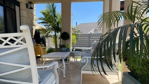 An outdoor patio area with white furniture, including a sofa and chairs, and a table. There are potted plants and a view of a building in the background. - Tavor View Suites (Galil Tachton)