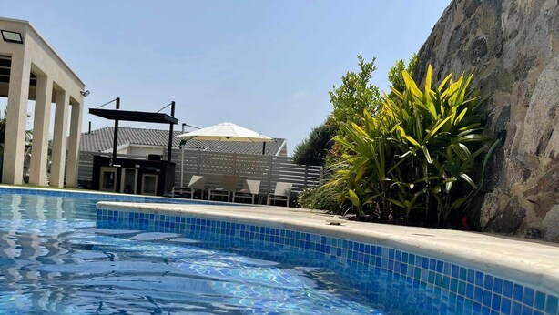 A swimming pool with clear blue water, surrounded by a tiled edge and a stone wall. - Tavor View Suites (Galil Tachton)