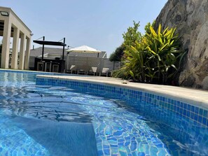 A swimming pool with clear blue water, surrounded by a tiled edge and a stone wall. - Tavor View Suites (Galil Tachton)