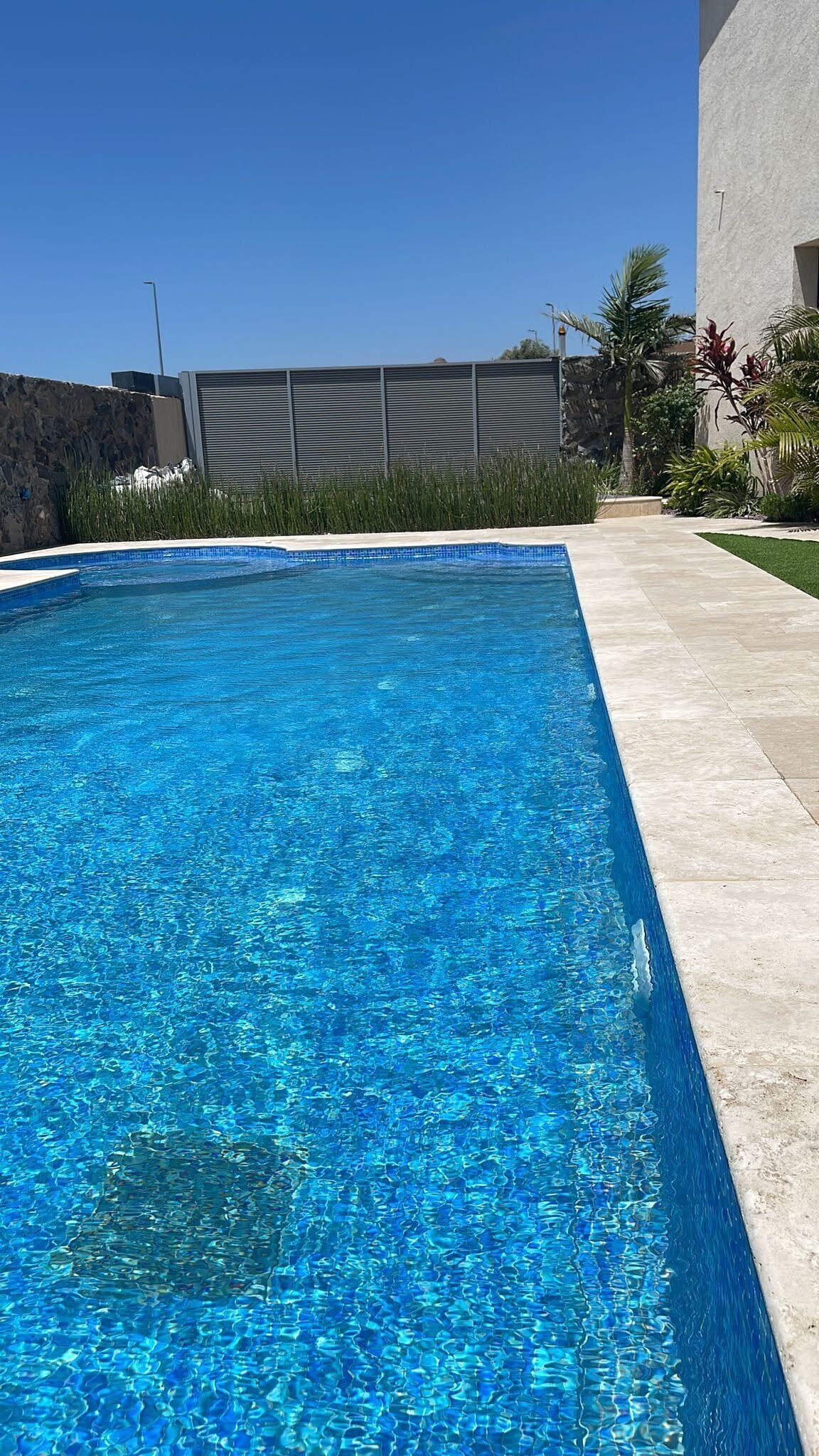 Une piscine rectangulaire à l’eau d’un bleu limpide, entourée d’un mur de pierre et bordée d’un chemin pavé.