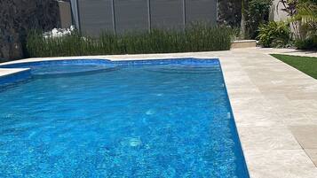 Une piscine rectangulaire à l’eau d’un bleu limpide, entourée d’un mur de pierre et bordée d’un chemin pavé.