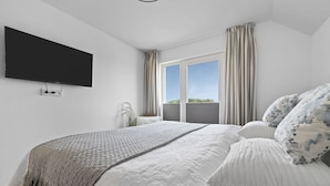 Une chambre moderne avec un grand lit, un téléviseur à écran plat fixé au mur et une fenêtre avec des rideaux.