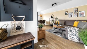 Un salon moderne avec un canapé, une table basse et un coin repas. On peut y voir des tableaux encadrés au mur, un luminaire suspendu et un panier posé sur le sol.
