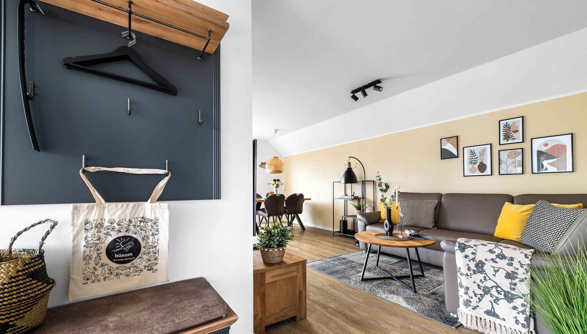 Un salon moderne avec un canapé, une table basse et un coin repas. On peut y voir des tableaux encadrés au mur, un luminaire suspendu et un panier posé sur le sol.