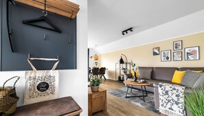 Un salon moderne avec un canapé, une table basse et un coin repas. On peut y voir des tableaux encadrés au mur, un luminaire suspendu et un panier posé sur le sol.