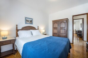 A bedroom with a bed, two bedside lamps, a wooden wardrobe, and a framed picture on the wall.