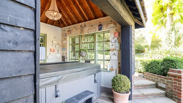 A cozy outdoor seating area with a wooden ceiling, a hanging chandelier, and a variety of signs on the wall. - Willow Cottage (Dartford)
