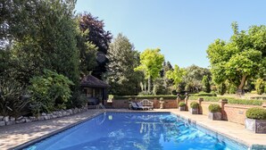A swimming pool with a clear blue water surface, surrounded by a brick patio and lush greenery. - Willow Cottage (Dartford)