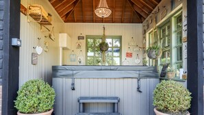 A cozy outdoor seating area with a bench, two potted plants, and a wooden ceiling. - Willow Cottage (Dartford)