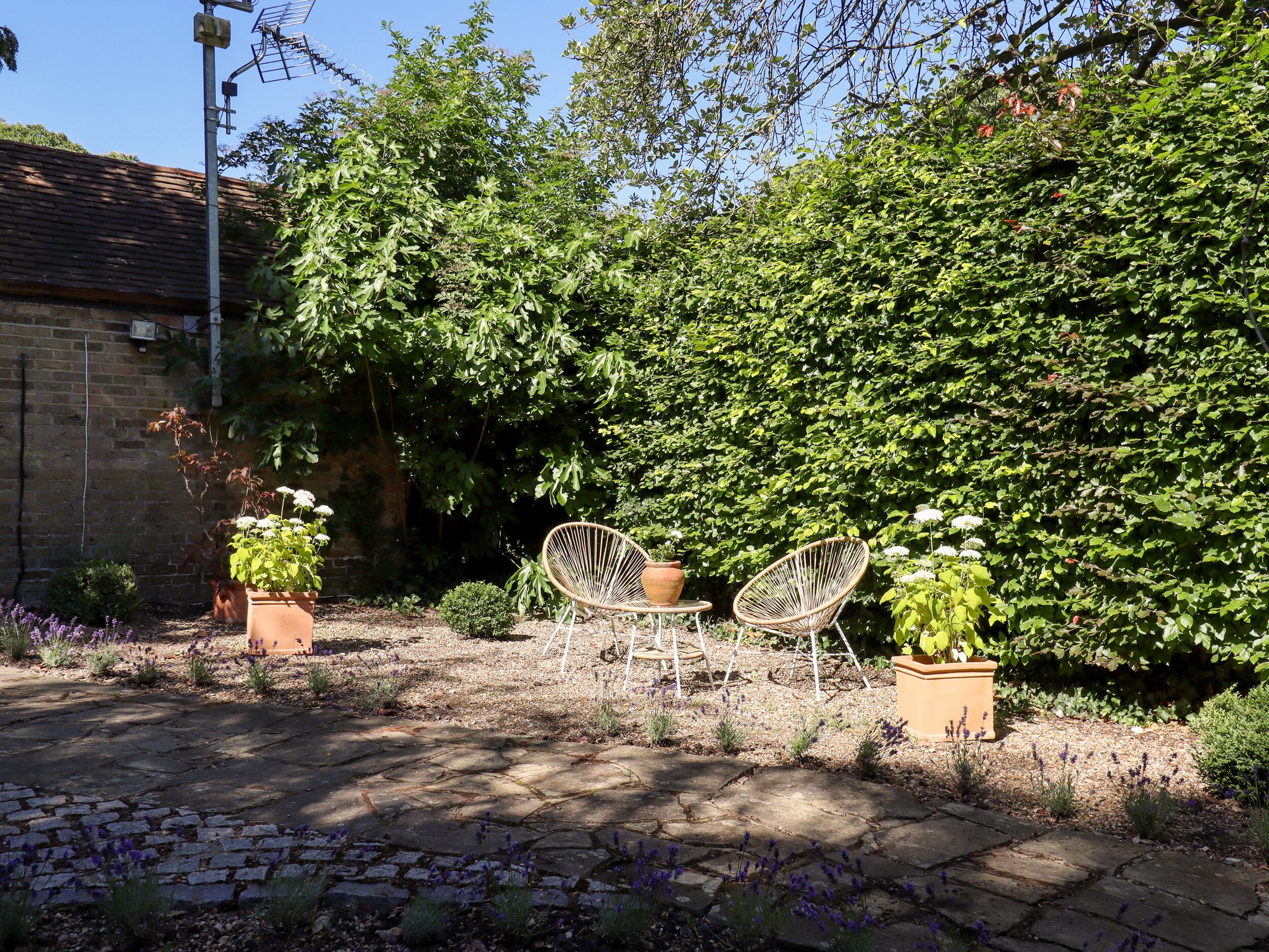 A garden patio with stone flooring, two wicker chairs, and potted plants.