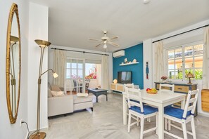 Een moderne woonkamer met een bank, een eettafel, een plafondventilator en een televisie.