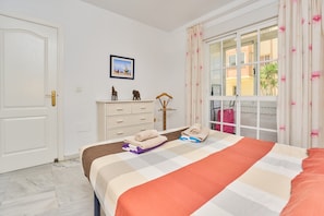 A bedroom with a bed, a dresser, a window with curtains, and a door. - Holiday Apartment Seafront with Sea View, Covered Terrace & Wi-Fi (Torrox)