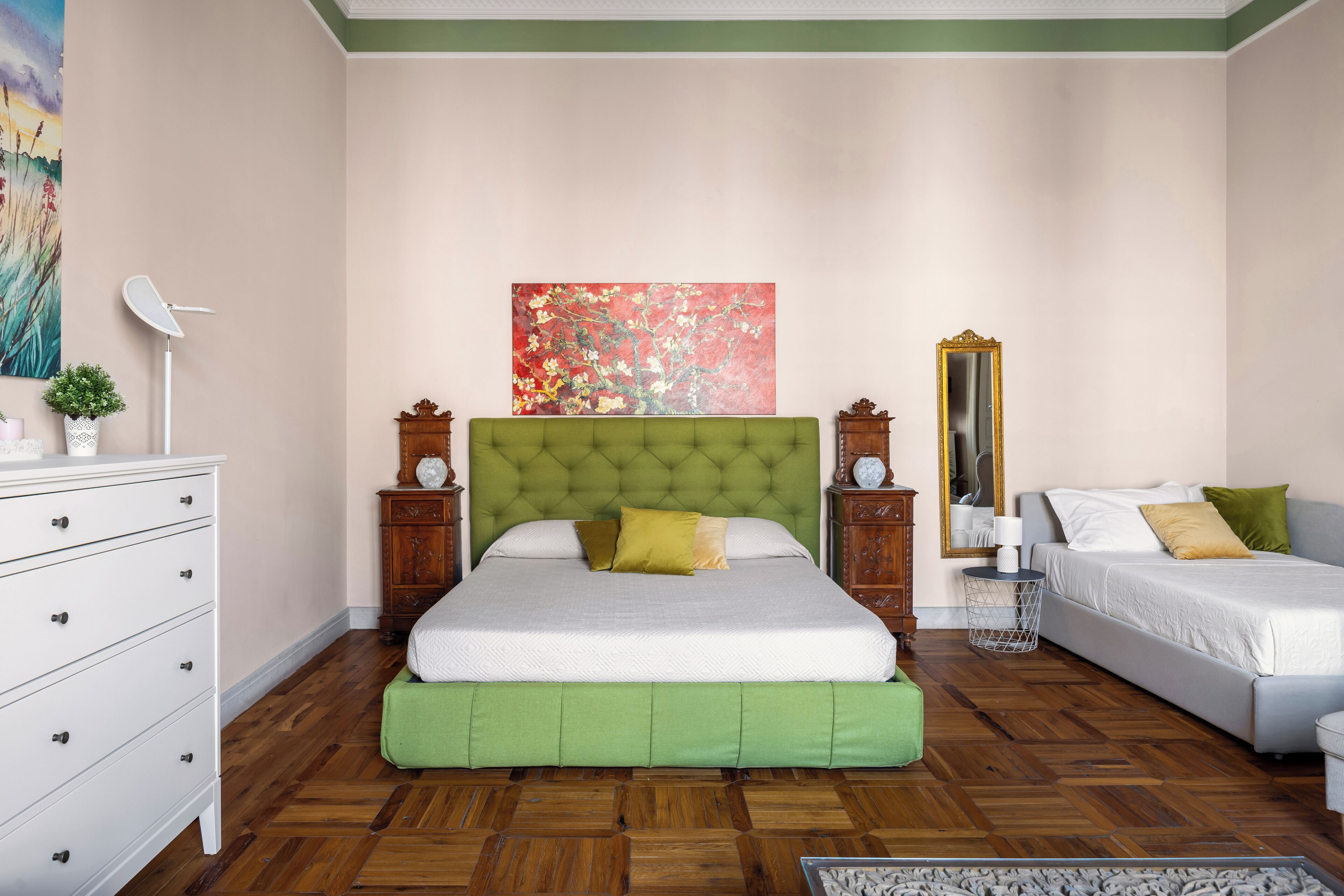 A bedroom with a green upholstered headboard, a large painting on the wall, a mirror, and a dresser.