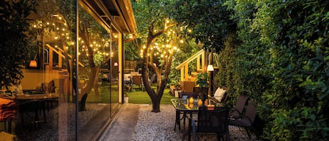 Un patio al aire libre con pared de vidrio, una mesa con sillas y luces colgantes.