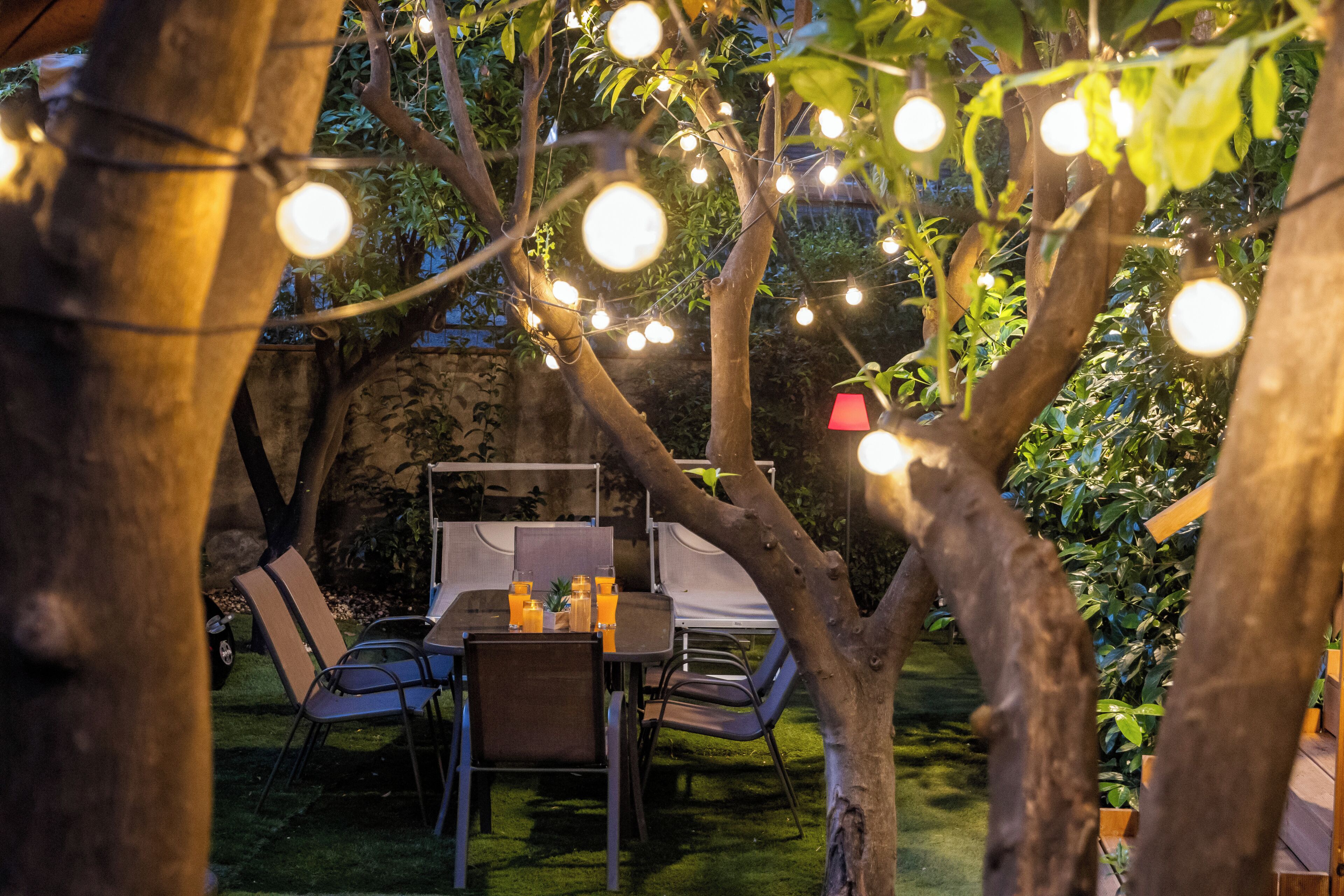 Un espace de restauration en plein air, avec une table et des chaises, entouré d’arbres et illuminé de guirlandes lumineuses.