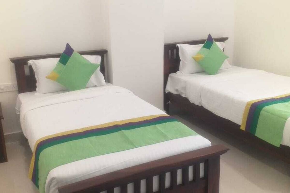 Deux lits simples avec des cadres en bois et une literie blanche, chacun agrémenté d’un coussin coloré et d’une couverture à rayures vertes et jaunes.