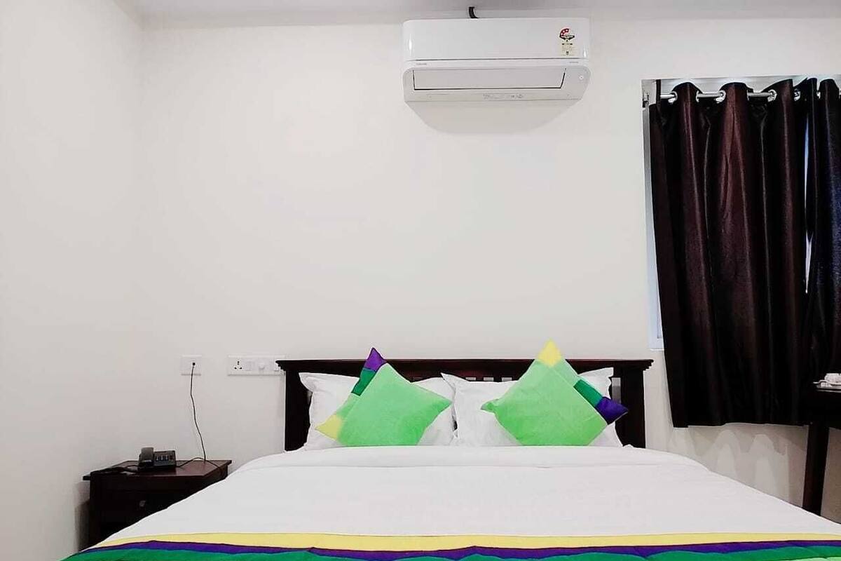 Une chambre d’hôtel avec un lit, une table de chevet, un appareil de climatisation et un rideau.