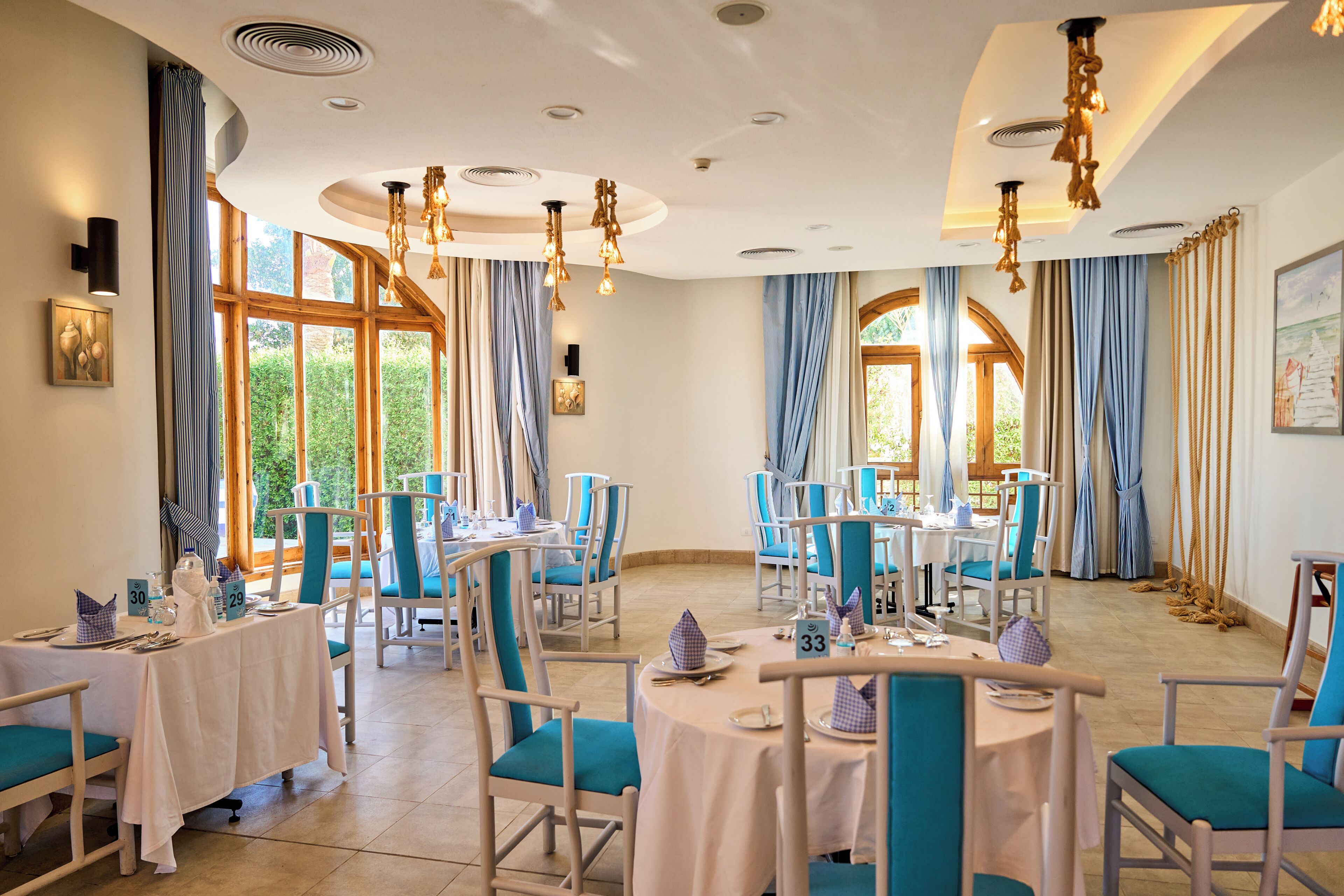 A dining area with tables and chairs, large windows, and a ceiling with recessed lighting.